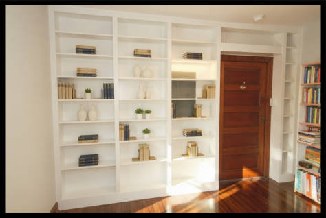 White Maple floor-to-ceiling wall-to-wall library featuring custom bridge bookcases over a bedroom entry door.